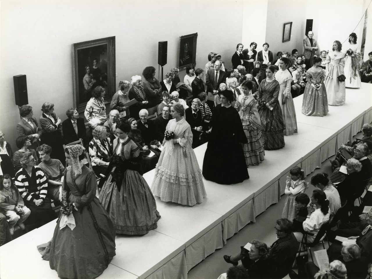 Zwart-witfoto van een modeshow in 1988 met de naam 'Ruisende Rokken' in het Centraal Museum, waarbij bezoekers kijken naar modellen gekleed in historische kostuums uit verschillende periodes die op de catwalk lopen.