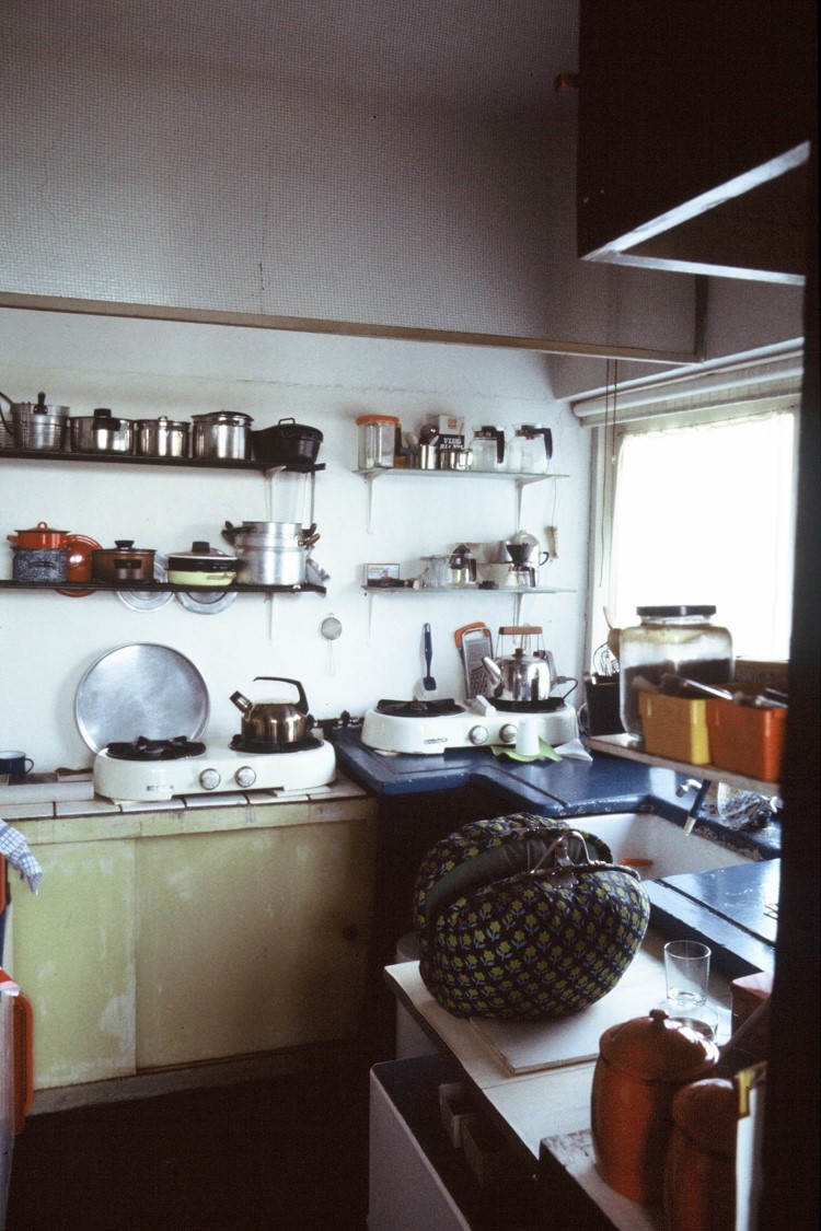 Een vintage keuken in het Rietveld Schröderhuis met retro kookgerei en pannen op schappen, twee kookstellen met waterkokers en een gevulde tas op het aanrecht.